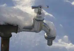 A metal outdoor faucet covered in snow, with a snowy background, highlights how East Tennessee weather impacts plumbing during the cold winter months.
