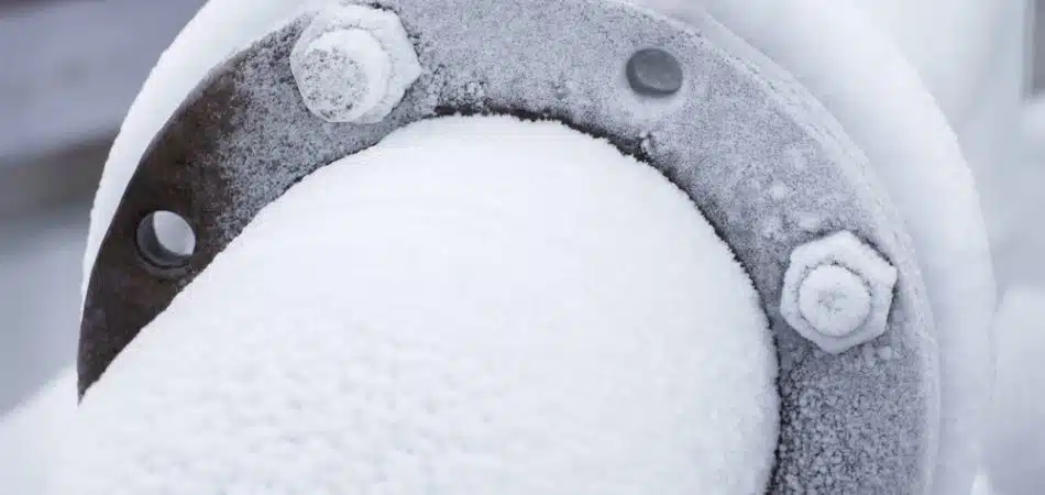A close-up of a metal pipe and flange covered with frost and ice, illustrating how East Tennessee weather impacts plumbing during cold snaps.