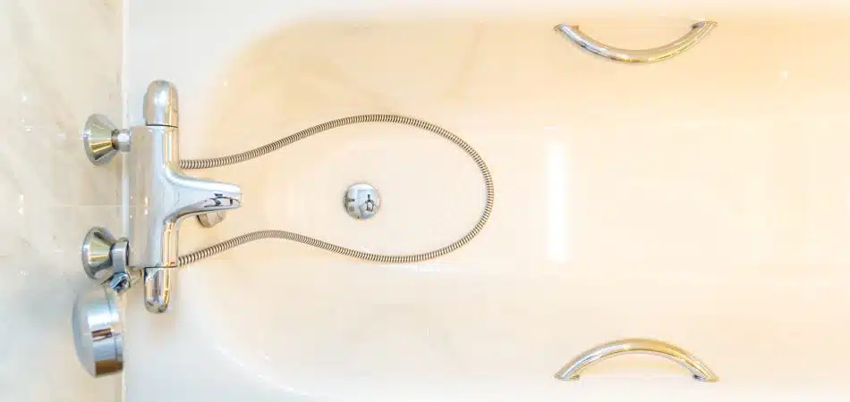 White soaking tub with chrome faucet, handheld shower hose, and safety grab bars viewed from above