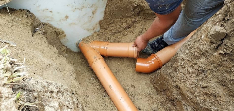 Worker installing orange sewer pipes in a dug trench