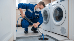 A plumber using a drain snake to clean a drain.