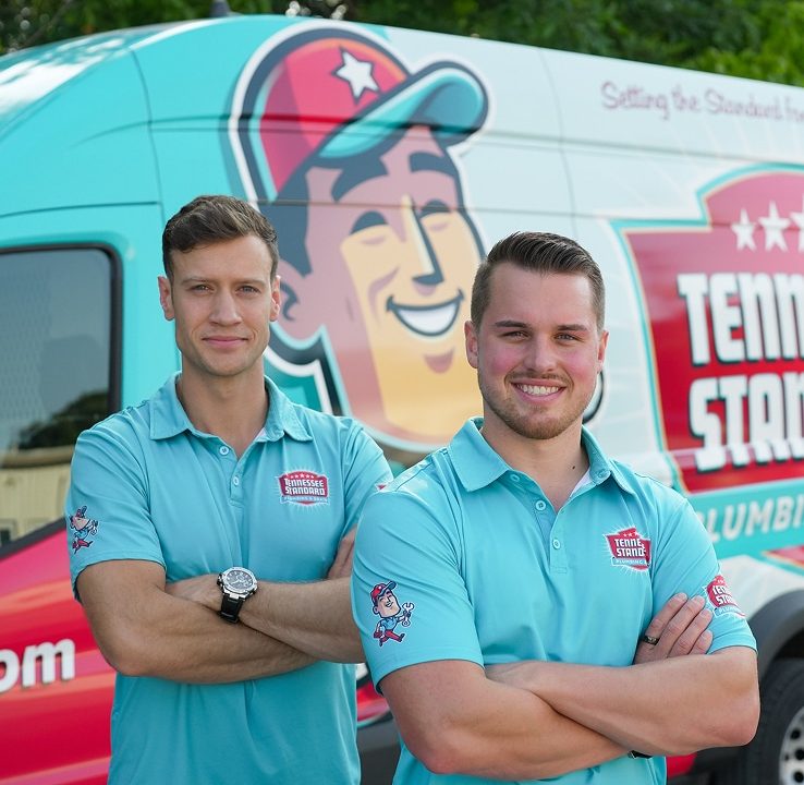 Bobby and Kelton Balka in light blue shirts stand smiling with arms crossed in front of a van displaying the Tennessee Standard logo and colorful graphics.
