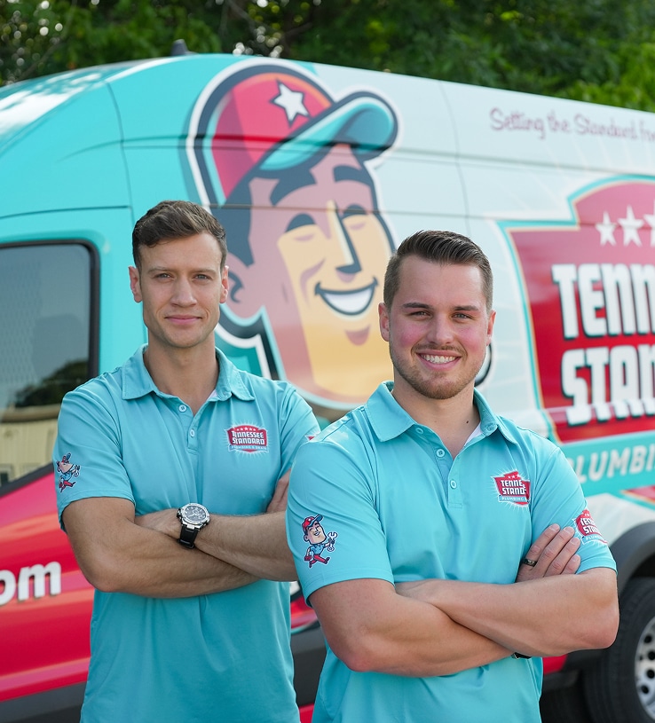 Bobby and Kelton Balka in light blue shirts stand smiling with arms crossed in front of a van displaying the Tennessee Standard logo and colorful graphics.