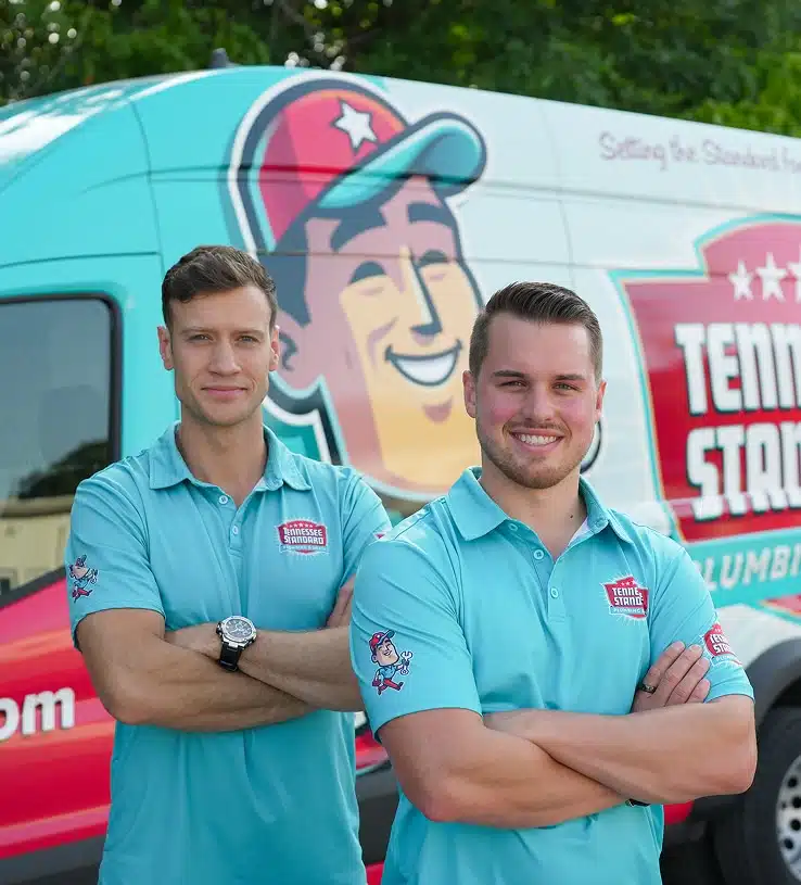 Bobby and Kelton Balka in light blue shirts stand smiling with arms crossed in front of a van displaying the Tennessee Standard logo and colorful graphics.