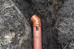 Orange PVC pipe with an angled joint installed underground, surrounded by soil—a typical sight when considering Sewer Line Repair vs. Replacement options.