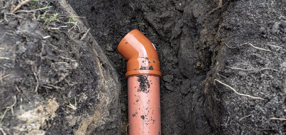 Orange PVC pipe with an angled joint installed underground, surrounded by soil—a typical sight when considering Sewer Line Repair vs. Replacement options.