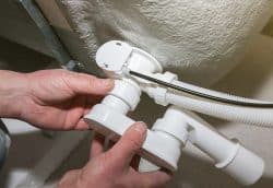 Person installing or adjusting white plastic Bathtub Drain pipes and fittings beneath a bathtub.