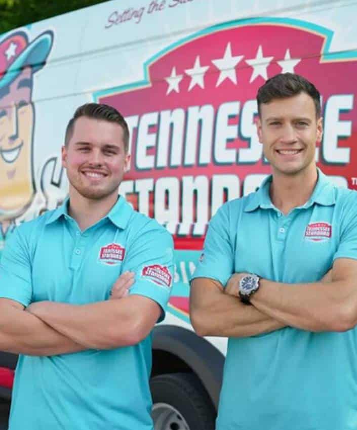 Bobby and Kelton wearing light blue polo shirts stand with arms crossed in front of a Tennessee Standard-branded van.