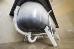 The underside of a bathtub showing exposed plumbing and a Bathtub Drain on a tiled bathroom floor.