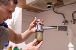 A person removes a dirty water trap from under a sink for cleaning or maintenance, an essential step during plumbing inspections for Oak Ridge homes.