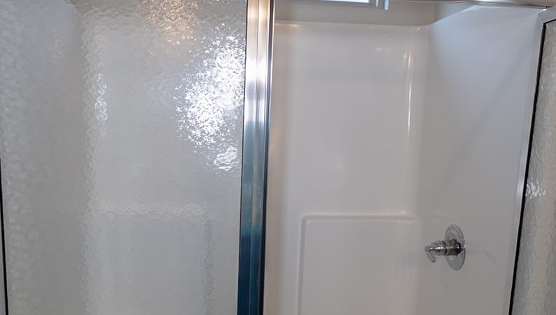 Glass shower with sliding door, chrome frame, and white fiberglass walls; showerhead and control handle visible on the right.