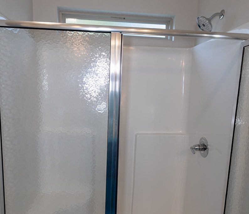 Glass shower with sliding door, chrome frame, and white fiberglass walls; showerhead and control handle visible on the right.