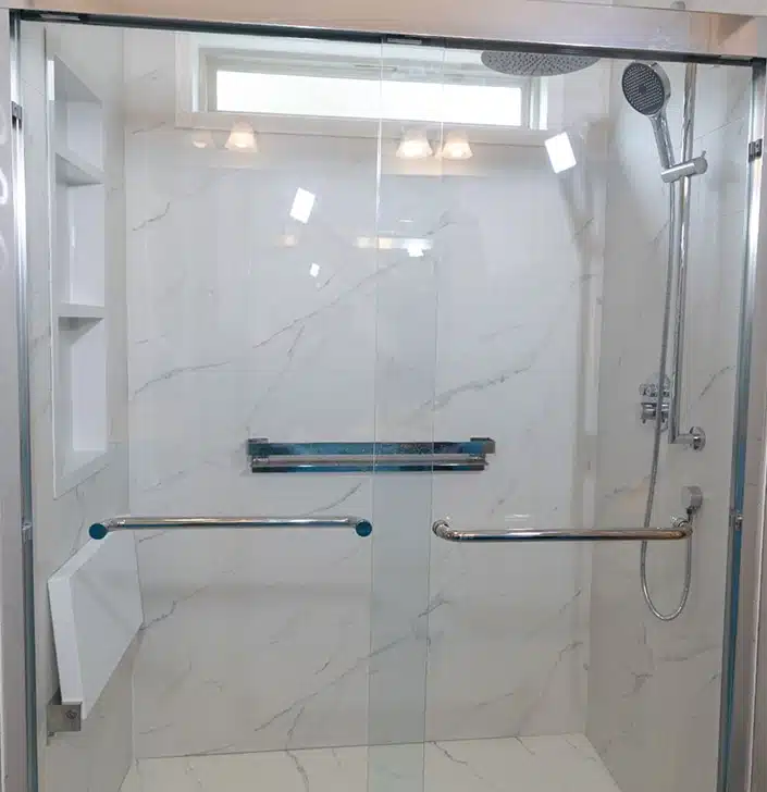 walk-in shower featuring a frameless glass door, white marble-style tiled walls, and built-in shelving