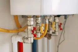 Close-up view of water heater pipes and valves in a utility room, featuring colorful connectors and tubes. Essential components for heating system maintenance and operation. Gas boiler taps.