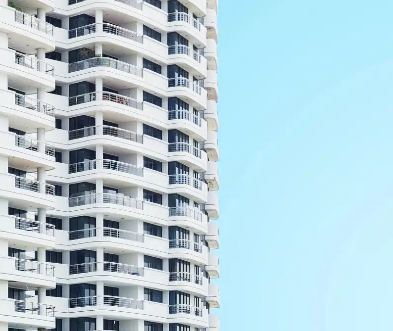 A modern high-rise apartment building with multiple balconies against a clear blue sky.