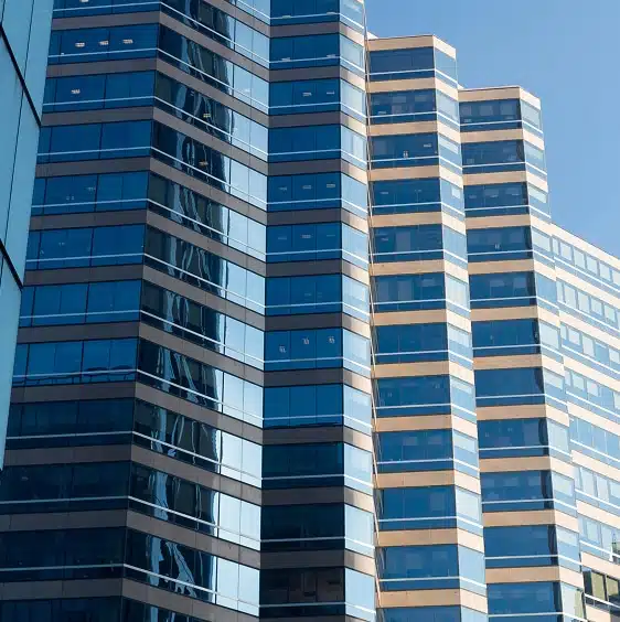 Close-up view of a modern glass office building with multiple stories and a blue sky reflected in its windows.