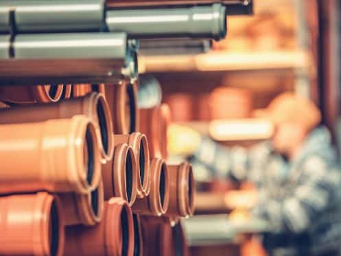 Close-up of stacked orange plastic pipes in a warehouse, with a worker in the background handling inventory—ideal for projects needing insight into professional drain repair costs in Knoxville.