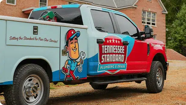 A Tennessee Standard Plumbing & Drain service truck is parked outside a brick house, featuring company branding and a cartoon plumber graphic on the side.