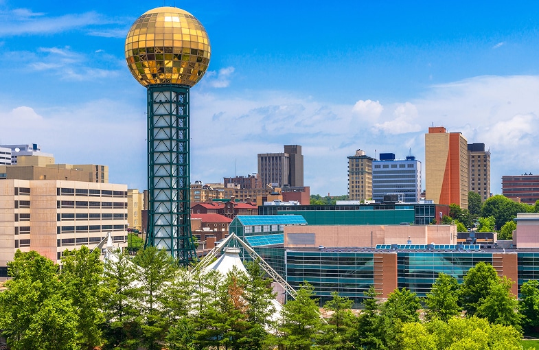 City skyline with a prominent golden sphere atop a tower, surrounded by modern buildings and lush greenery under a clear blue sky in Corryton