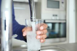 A person holds a glass under a running faucet, filling it with water in a kitchen setting, demonstrating the benefits of Water Treatment Systems Knoxville.