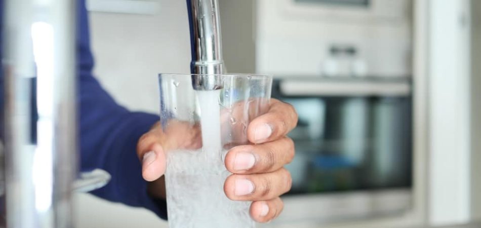 A person holds a glass under a running faucet, filling it with water in a kitchen setting, demonstrating the benefits of Water Treatment Systems Knoxville.