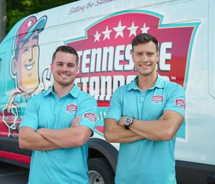 Bobby and Kelton Balka wearing a light blue shirts stand smiling with arms crossed in front of a van displaying the Tennessee Standard logo and colorful graphics.