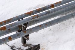Three parallel metal pipes with rust spots are mounted on a support structure, surrounded by snow—a reminder to follow essential plumbing maintenance tips during winter months.