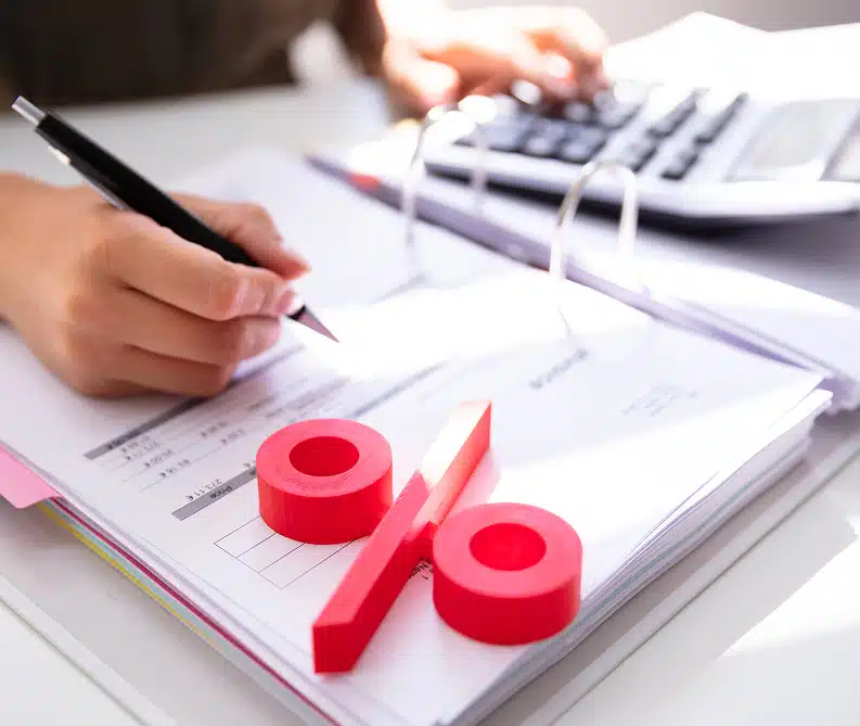 Person using a calculator and writing in a binder, with a large red percentage symbol placed on the papers.