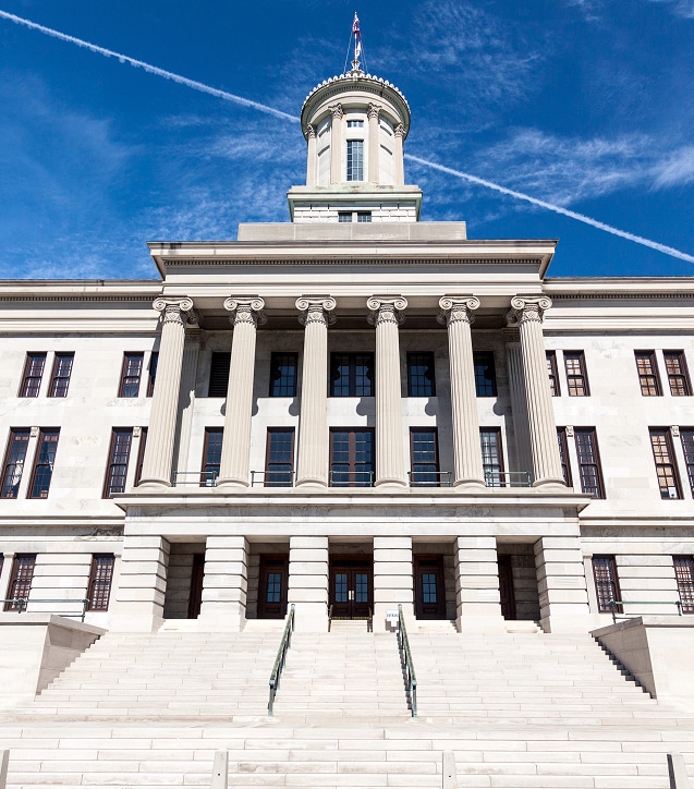 A neoclassical government building with tall columns, wide stone steps, and a central tower against a blue sky.
