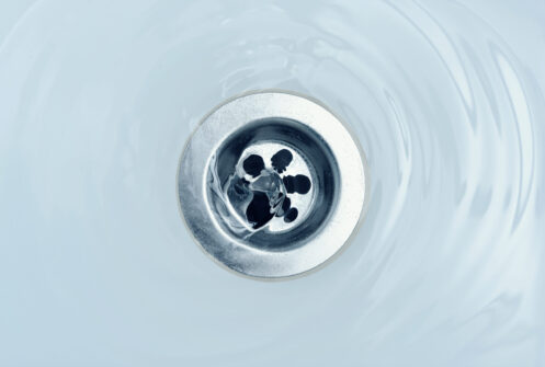 Water flowing from a sink drain, creating ripples in the basin below.