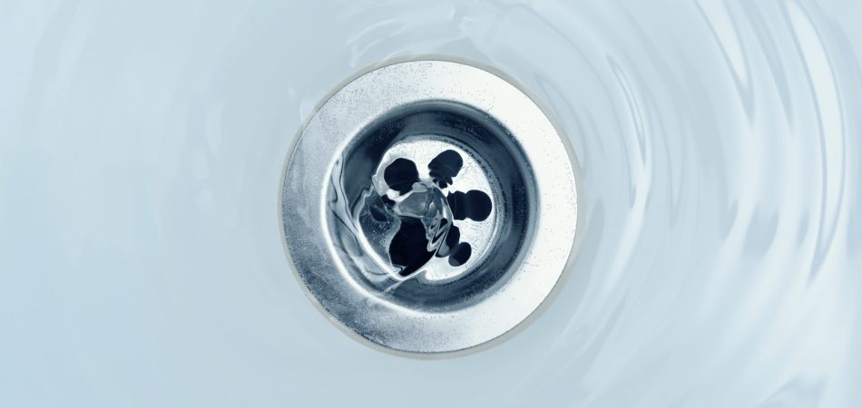Water flowing from a sink drain, creating ripples in the basin below.