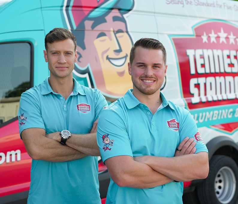 Bobby and Kelton in matching teal polo shirts stand with arms crossed in front of a van with a colorful