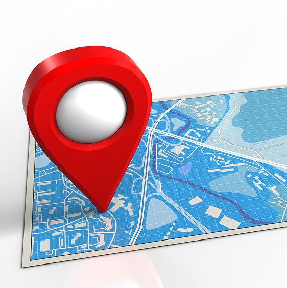 A large red map pin is placed on a printed map with blue and white details, indicating a specific location.