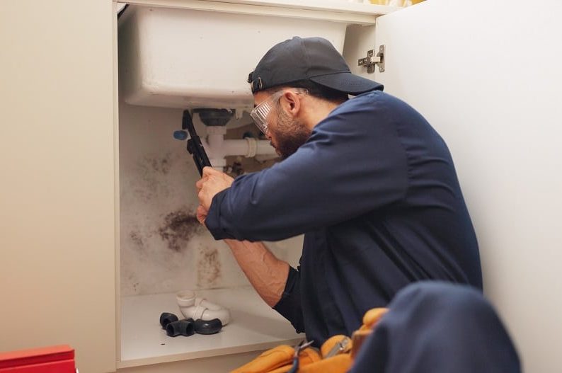 Plumber, man and tools for pipeline in kitchen with home maintenance service and fixing leak by sin.