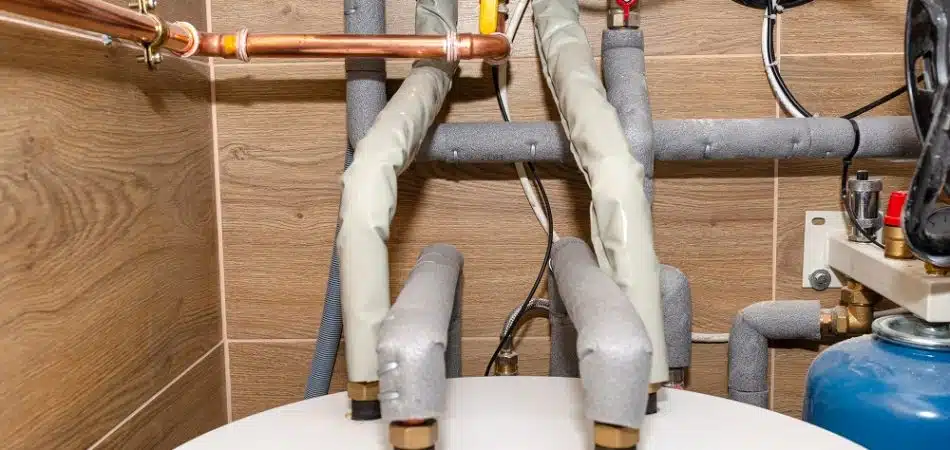 Water tank and gas pipes for a modern gas boiler in a home boiler room, lined with ceramic tiles.