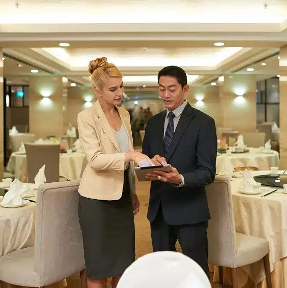 Two business professionals standing in a restaurant, looking at and discussing information on a digital tablet.