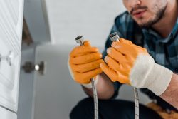 selective focus of handyman holding metal hose near kitchen cabinet