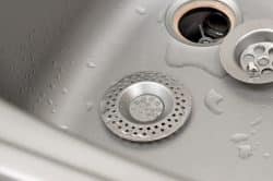 Close-up of a kitchen sink with water droplets, featuring a metal drain strainer and removed drain cover—ideal for illustrating the process of installing kitchen sink drain components.