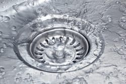 Close-up of water flowing into a stainless steel sink drain with bubbles forming around the drain, highlighting proper drainage and essential Plumbing Maintenance Tips.