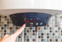 A hand presses the power button on a Water Heater in Oak Ridge featuring a digital temperature display and control buttons below.
