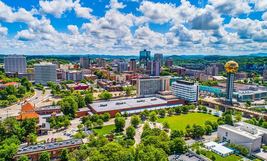 Aerial view of a cityscape with modern buildings, green trees, and a prominent golden sphere structure under a partly cloudy sky.
