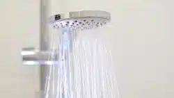 Close-up of a modern handheld showerhead spraying water, mounted on a metal rail against a plain background—a common sight when hot water runs out fast in Maryville.