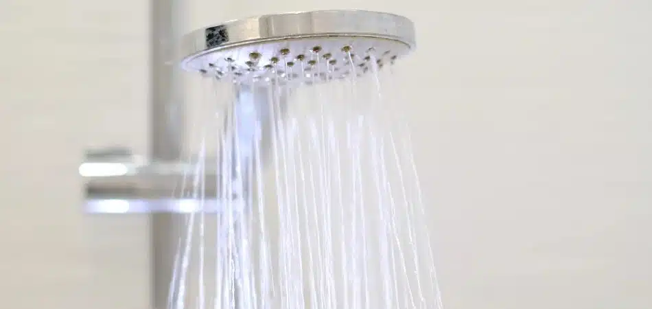 Close-up of a modern handheld showerhead spraying water, mounted on a metal rail against a plain background—a common sight when hot water runs out fast in Maryville.