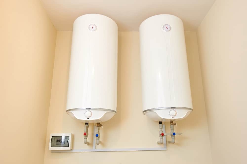 Two white cylindrical water heaters are mounted side by side on a beige wall in Oak Ridge, with pipes and a digital control panel below them.