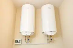 Two white wall-mounted water heaters with pipes and a control panel are installed on a beige wall—ideal for addressing inconsistent hot water in Knoxville homes.