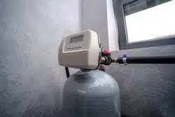 A water softener unit with a digital control panel sits atop a gray tank.
