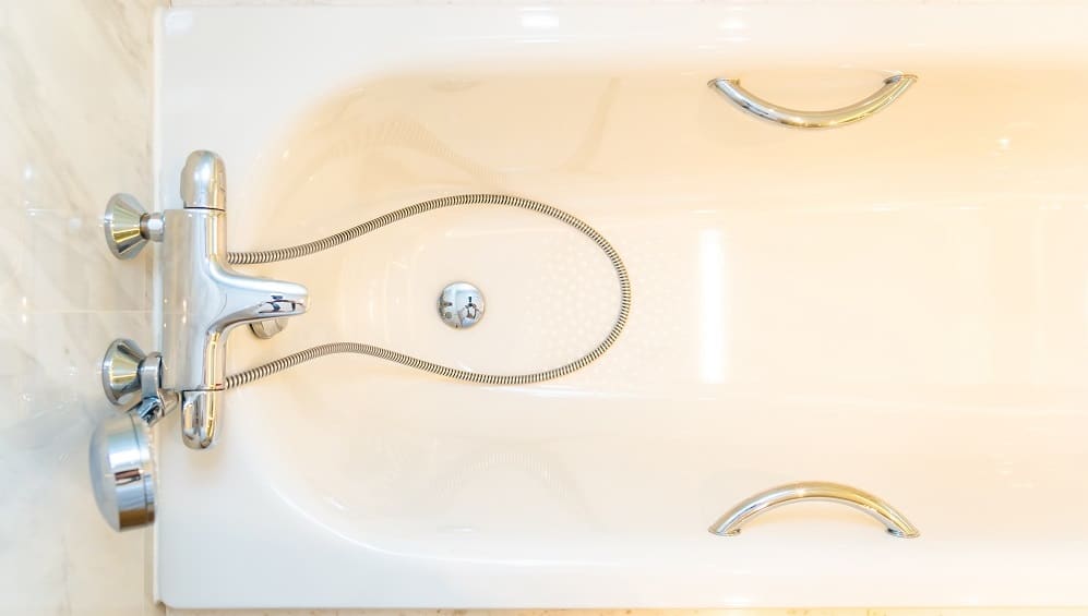 Overhead view of an empty white bathtub with chrome handles, a silver faucet, and a flexible shower hose resting inside near the bathtub drain.