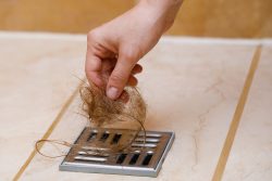 Woman removing hair clump from the shower drain. Cleaning or hair loss concept.