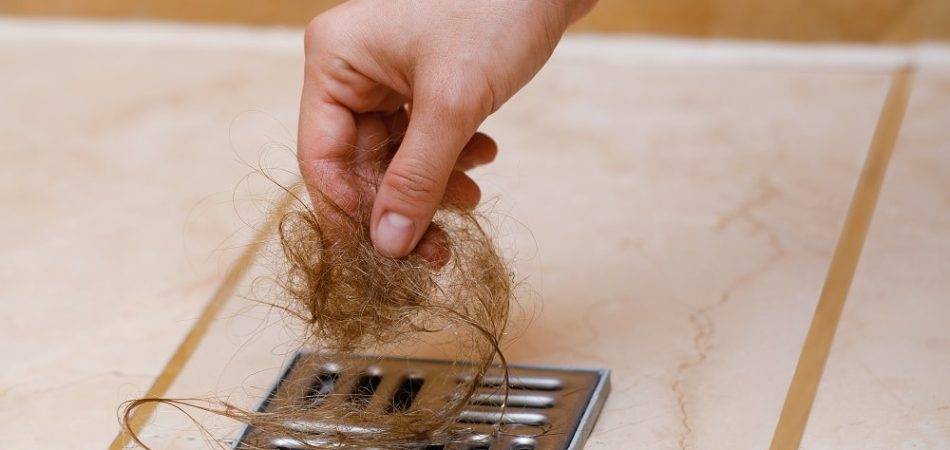 Woman removing hair clump from the shower drain. Cleaning or hair loss concept.