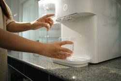 Woman using water purifier marble countertop in a home kitchen. Hydration, health and convenience concept.